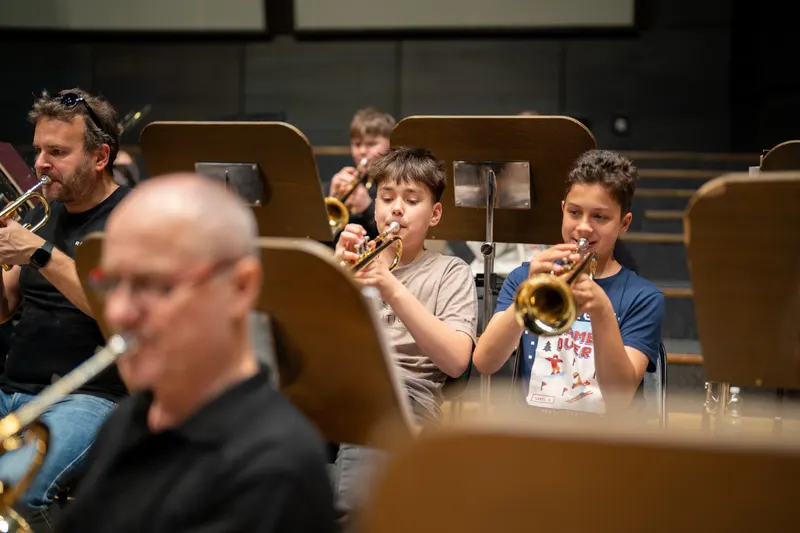 Zkouška dechového orchestru, v popředí trubka, za ní mladí trumpetisté